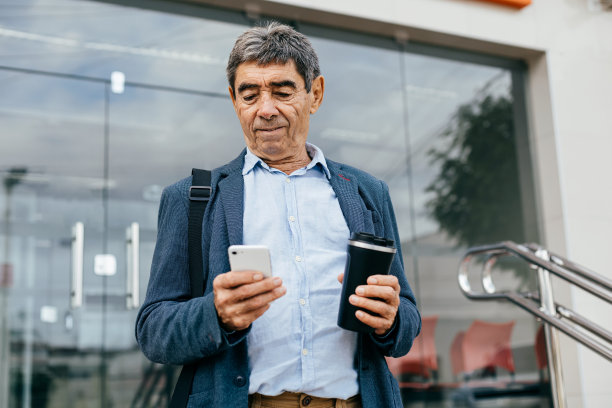 一位杰出的70岁商人在城市里用手机自信地管理着商业事务图片下载