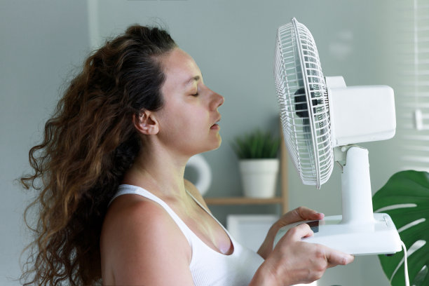 女人享受电风扇，在家里，在炎热的夏天冷却他的脸图片下载