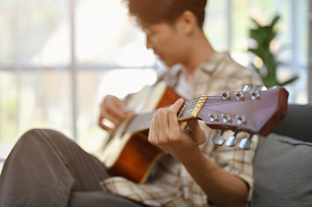 一个放松的亚洲人坐在客厅的沙发上弹吉他的特写。图片下载