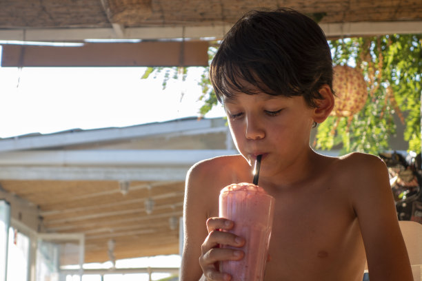 小男孩在沙滩上喝奶昔鸡尾酒。图片下载