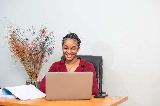 一个快乐的非洲女人坐在桌子前用笔记本电脑工作。图片下载
