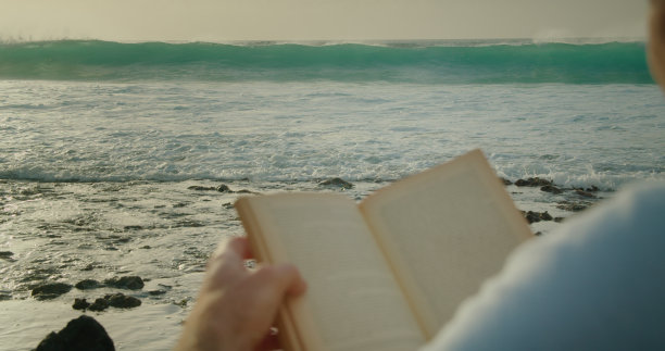 一个人在沙滩上悠闲地看书。背景是暴风雨般的海浪。图片下载