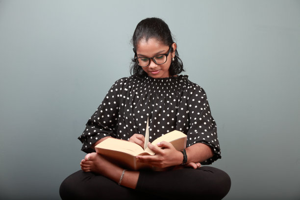 年轻的印度女孩坐在莲花姿势和看书图片下载