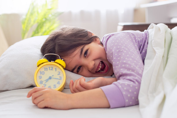 可爱的情绪深黑色的女孩穿着紫色的睡衣躺在白色的枕头上，在床上，在晨光中，笑着图片下载