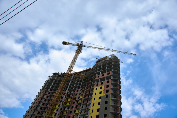 在蓝天白云的映衬下，塔吊正在建造一座高层建筑图片下载