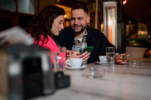 年轻的夫妇坐在咖啡馆用手机预订图片下载