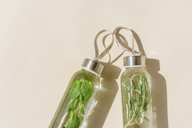 水喝排毒与绿色迷迭香叶在玻璃瓶在阳光米色背景。养生、饮食、饮食健康的理念。时尚的玻璃可重复使用的水瓶，生活方式的最小照片图片下载