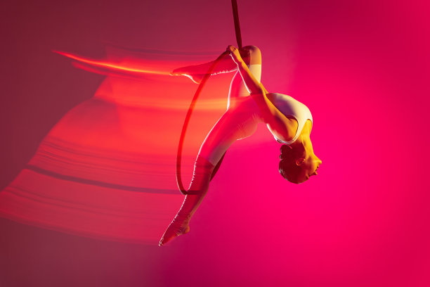 年轻灵活的女孩，专业的空中体操训练，表演孤立的粉红色背景与混合灯光的效果图片下载