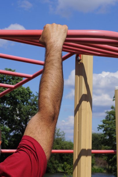男运动员的一只手放在运动单杠的红色铁管上图片下载