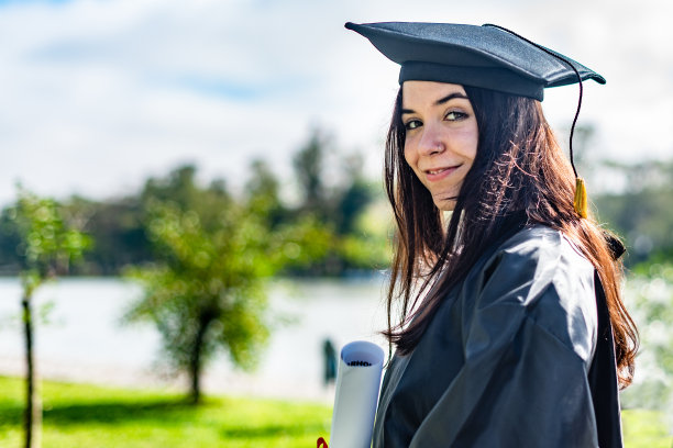 快乐的白人毕业女孩与棕色长发，拿着文凭，看着相机图片下载