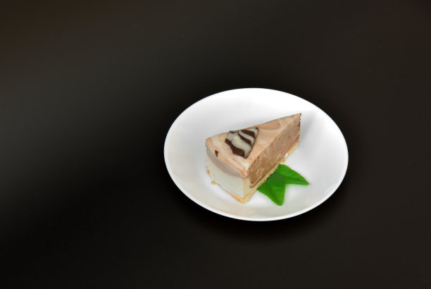 圆形的白色陶瓷盘子上有一块新鲜的奶油芝士蛋糕，黑色背景上有薄荷叶。图片下载