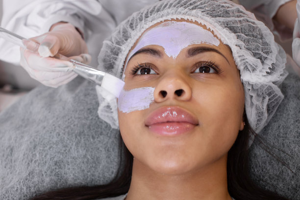 美容。美容师用刷子在黑人女性脸上涂抹清洁面膜。图片下载