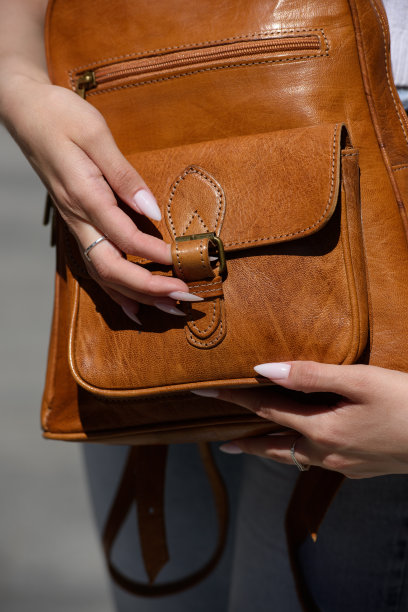 一个穿着白色紧身裤和t恤的女孩，手里拿着一个浅棕色的皮革背包图片下载