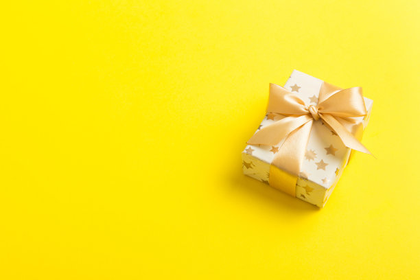 用白色包装纸包装圣诞节或其他节日手工制作的礼物，并在彩色背景上系上金色丝带。礼品盒，彩色桌子上的礼品装饰，顶部视图与复制空间图片下载