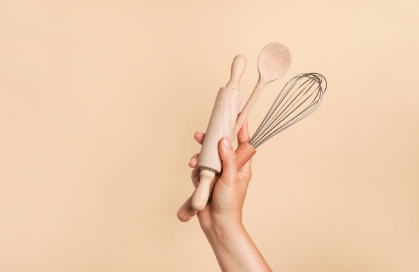 米色背景的女性手拿着厨房食品和烘焙用具。搅拌，擀面杖和木勺图片下载