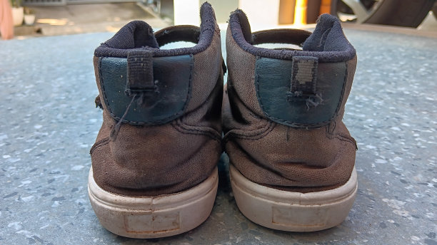 一个男孩的旧的和磨损的黑鞋的正面视图图片下载