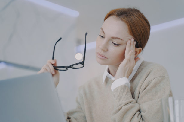 精疲力竭的年轻女子在办公室有太阳穴疼痛。劳累过度的女孩摘下了眼镜。图片下载