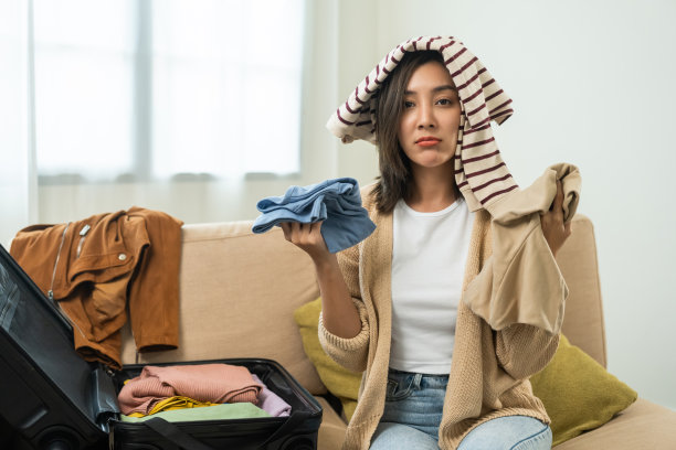 快乐美丽的女人叠好她的衣服，装好旅行箱，准备假期旅行。年轻女性在家里整理行李时叠衣服。图片下载