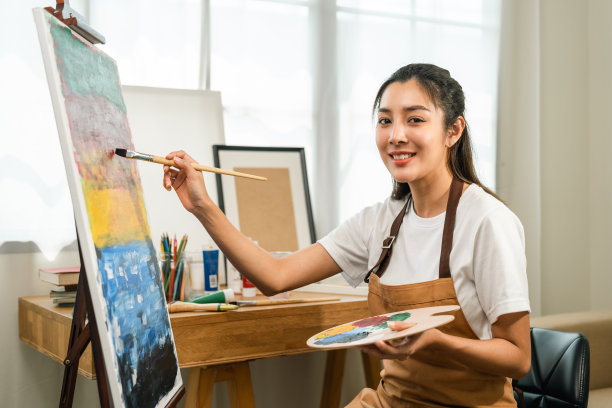 亚洲女艺术家正在用画笔和不同的丙烯酸颜料作画。作为艺术概念的女艺术家在创作工作室的画布上作画图片下载