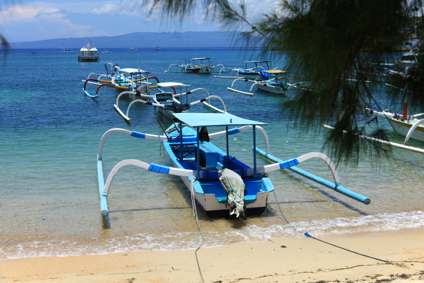 东巴厘岛的Padangbai海滩上有许多小型摩托艇、perahu渔船和游船停泊在白色的沙滩上或绿松石色的海水中。背景中可以看到Nusa Lembongan岛。图片下载