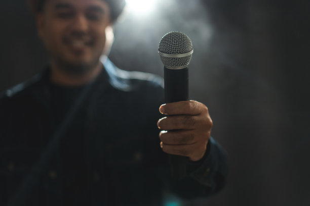 吸引人的歌手在舞台上唱歌和弹吉他的特写镜头，聚光灯穿过音乐会的黑暗。音乐家在大厅里用灯光和烟雾现场表演。图片下载