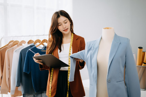 时装设计师女士在现代工作室里讲智能手机，用笔记本电脑和数码平板电脑，衣服挂在架子上图片下载