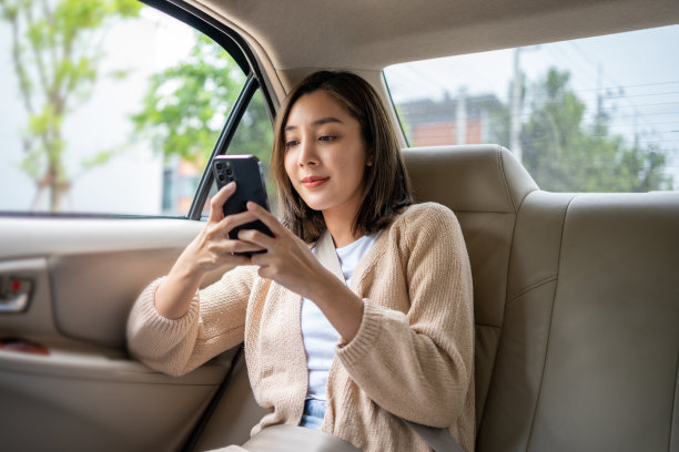 美丽的女人坐在汽车后座上，用智能手机玩社交媒体，系上安全带，看着窗外的放松时刻。女快乐地在车里行驶在通往目的地的路上。图片下载