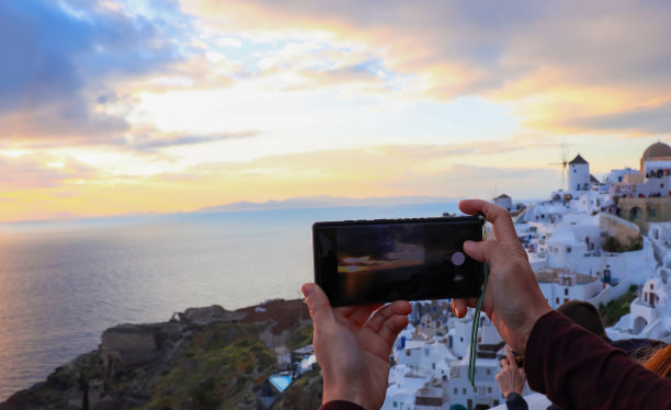在希腊圣托里尼岛的伊亚村，一名年轻的游客用智能手机在蓝色的教堂圆顶前拍照图片下载