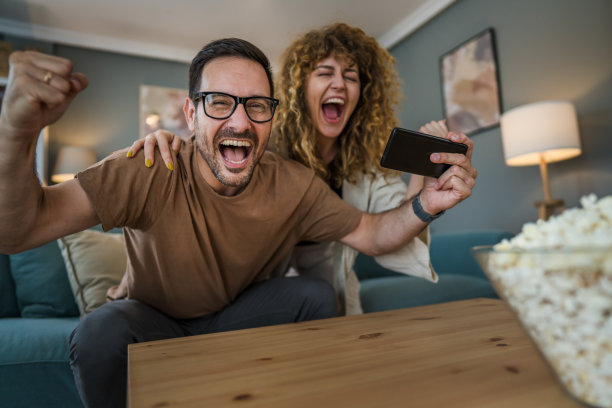 一对夫妻，丈夫和妻子在家里玩智能手机视频游戏图片下载