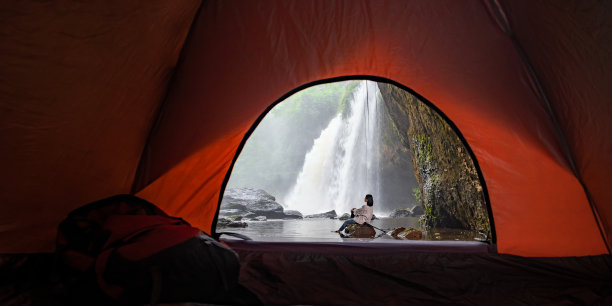 亚洲女游客们在森林中的洞穴里露营，体验泰国热带森林地区的瀑布氛围。一个亚洲女人为了看美丽的瀑布而露营。图片下载