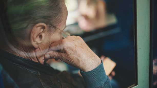 特写，沉思的老人在乘坐火车时使用手机，透过玻璃观看图片下载