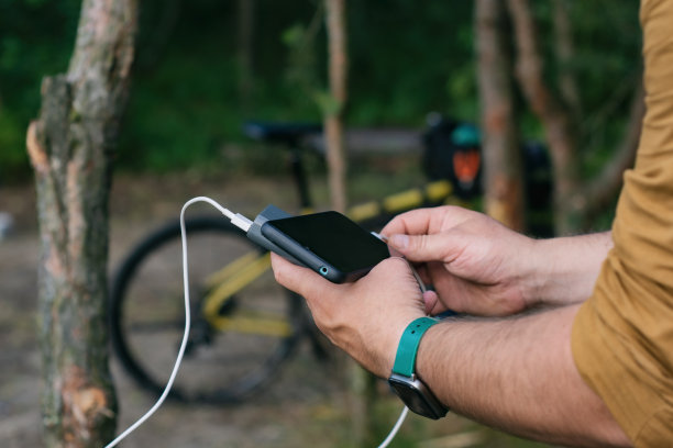 一名游客在森林里骑自行车，用充电宝给智能手机充电。图片下载