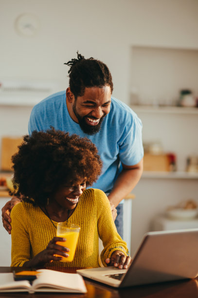 一对快乐的非裔美国夫妇看着笔记本电脑，在家里开怀大笑。图片下载