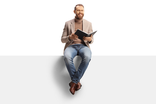 微笑的年轻人拿着一本书，坐在一个空白的面板上图片下载