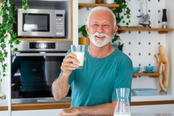老人喝着一杯牛奶，满脸笑容地站在那里。帅气的老人在厨房里喝着一杯鲜牛奶图片下载