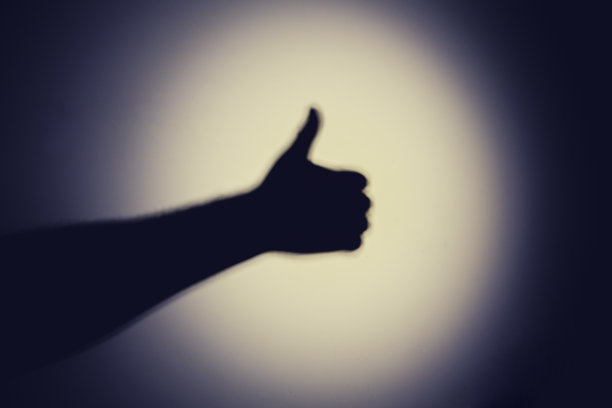 在白色的墙上，手电筒的夜光投射出一只手的影子。灯光下一个男人的黑色剪影图片下载