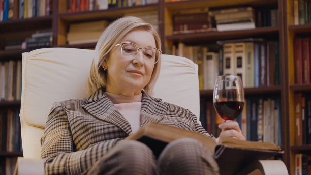 50多岁的有钱女人，一边读书一边喝酒，在家里的图书馆里休息图片下载