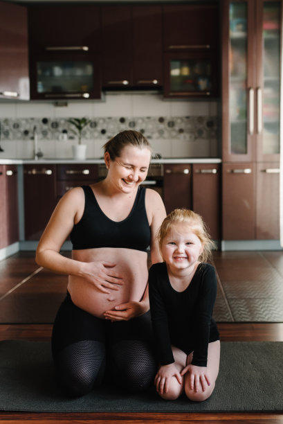 孕妇和孩子穿着运动服在家里锻炼。大肚子的雌性。家庭瑜伽概念。孕期瑜伽和健身。母女俩训练，一起打坐，坐在垫子上图片下载
