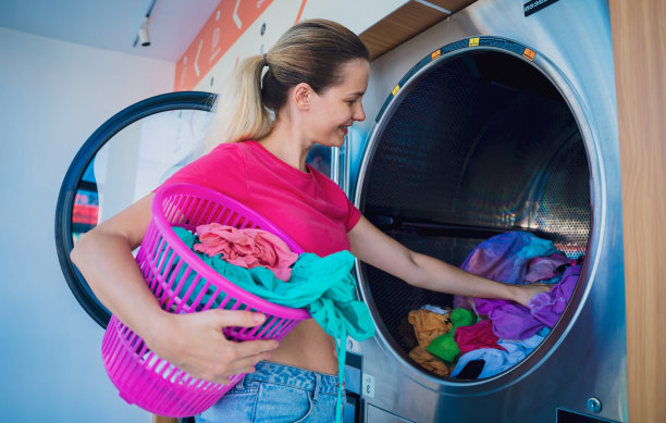 年轻漂亮的女人在洗衣房洗衣服和烘干衣服图片下载