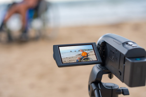 一个坐在轮椅上的残疾人在沙滩上录制视频图片下载