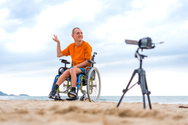 一个坐在轮椅上的残疾人在海滩旁录制视频图片下载