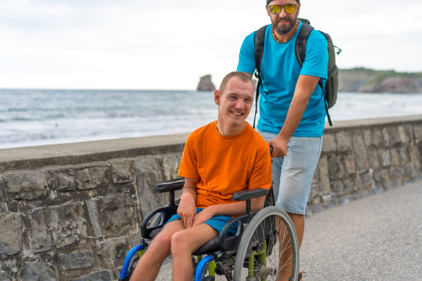 一个坐在轮椅上的残疾人被朋友推在沙滩上，在夏天玩得很开心图片下载