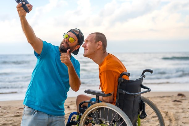 一个坐在轮椅上的残疾人和朋友在沙滩上自拍图片下载
