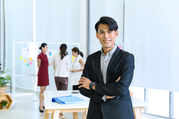 一个自信的商人双臂交叉站在办公室的桌子前。把想法带到通往成功的道路上。图片下载