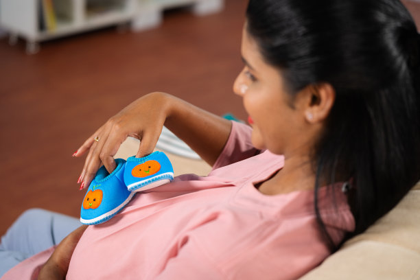 印度孕妇在家里玩婴儿鞋或婴儿靴的肩部照片-产前联系，母性和怀孕快乐的概念图片下载