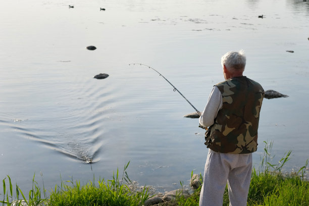 老人钓鱼。夕阳西下，一位白发苍苍的老渔夫从码头上抛下一缕丝线。积极的老年男性在湖中垂钓，旋转卷轴杆。退休渔民享受他的周末图片下载