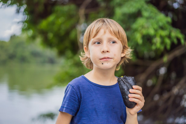 男孩吃着夹在黑色长棍面包里的越南叉烧三明治图片下载