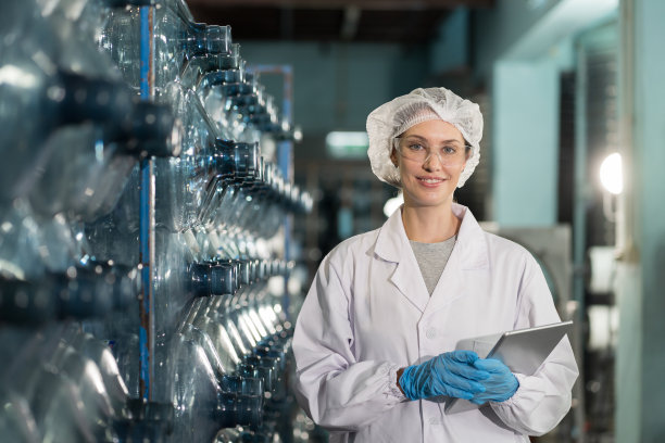 在矿泉厂用数码平板检测塑料饮用水箱质量的女工。女工在装瓶过程中检查塑料加仑图片下载