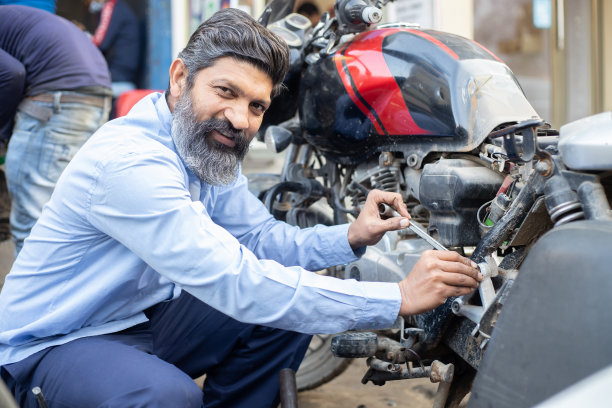 专业的印度技工用螺丝刀修理摩托车。一名亚洲男子在修理店修理摩托车。图片下载