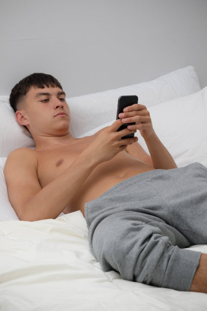 赤膊少年在床上玩手机图片下载